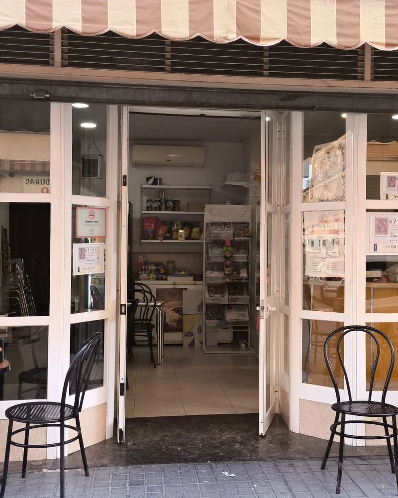 Fachada del local con el toldo, la puerta abierta y las sillas de la terraza.